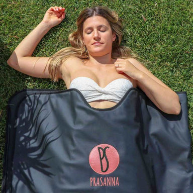 A blonde woman lying down and enjoying her sauna blanket. Her yes are close. The sun is bright