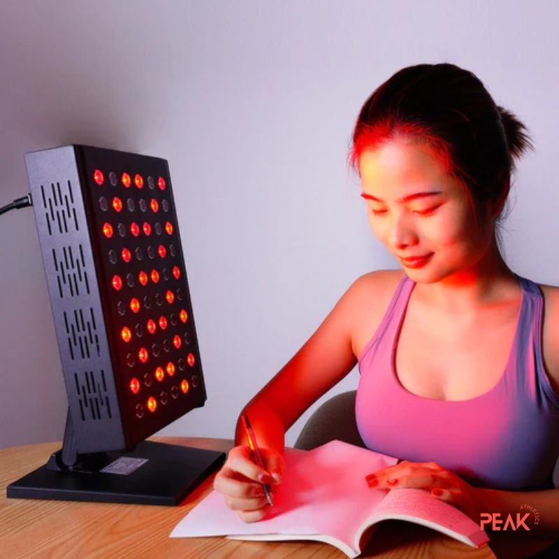 An image of a woman enjoying a red light therapy session while she holds a pen and a piece of paper, it seems she writing down something. The red lights are on. The room is dark
