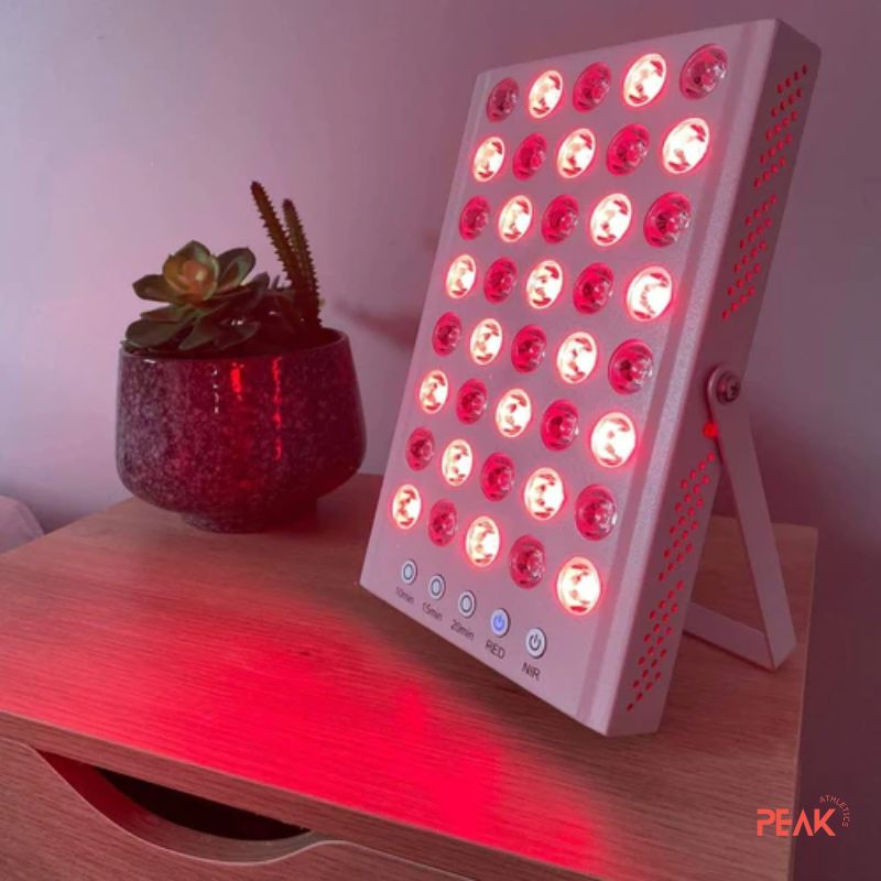 A photo of the PowerPanel mini with the lights on. The red light panel is on a small bed side table. There is also a small plant near by. 